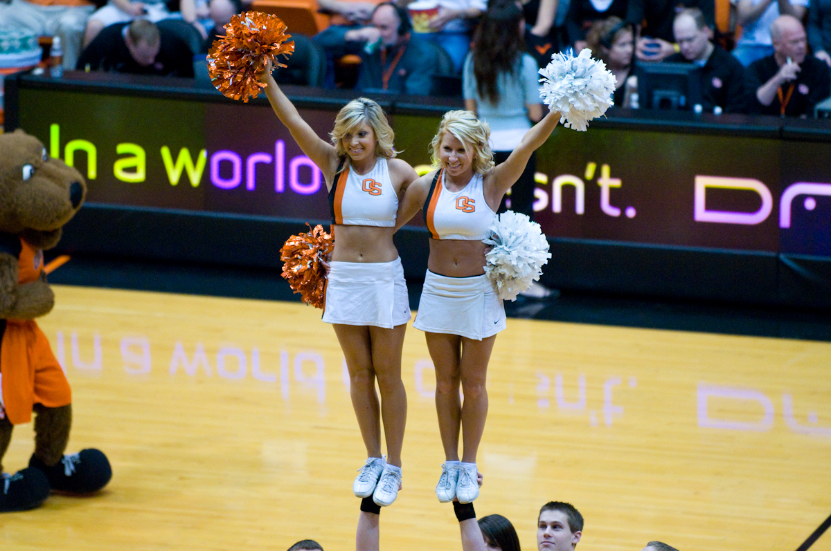 two girls in cheerleader outfits are on a basketball court while an animal is behind them