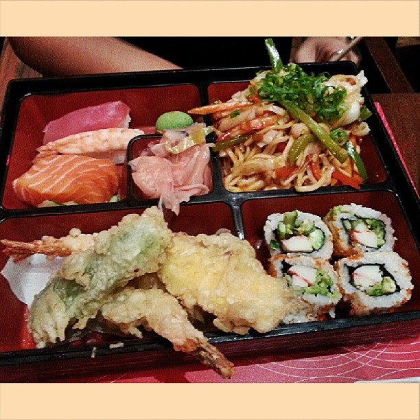 a tray of food that includes shrimp, pasta, sushi and salad