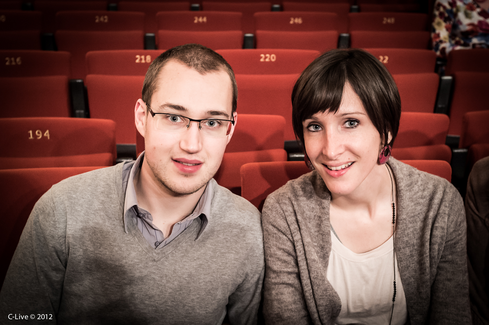 a couple with glasses sit on red chairs