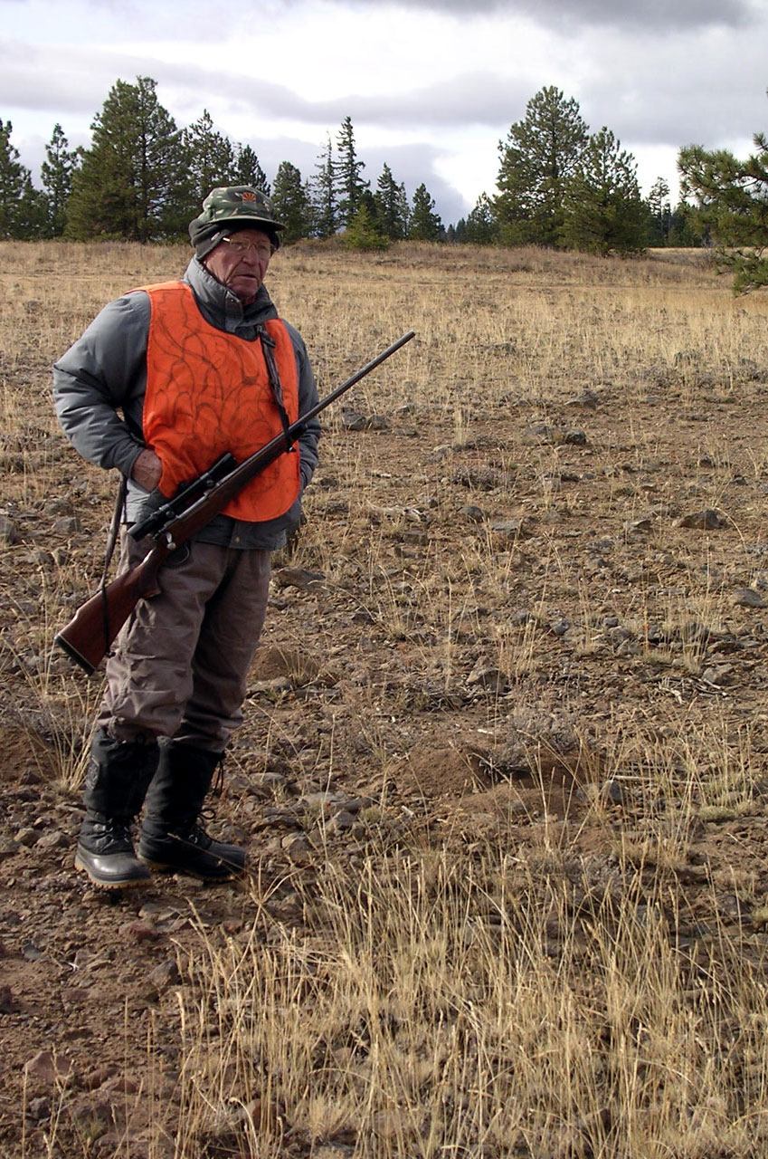 an elderly man holds a rifle in a field