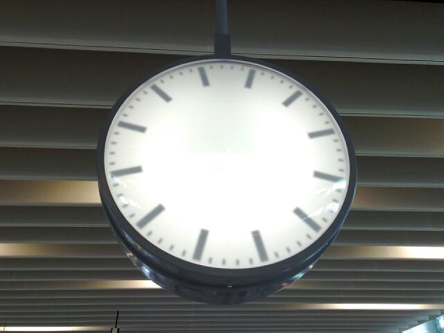 a round illuminated clock hanging from a ceiling