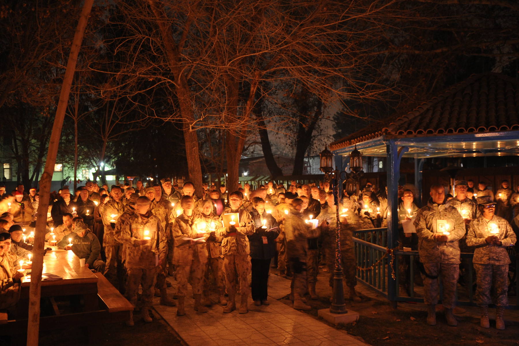 many men and women dressed in us military fatigues light candles as they stand in a park