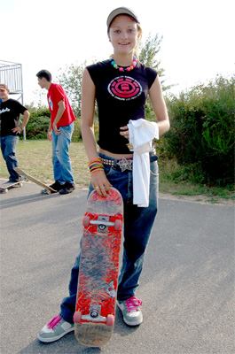 a woman is holding a skateboard standing on the side of the street