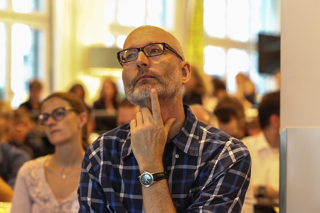 a man and woman in front of an audience, one is wearing glasses