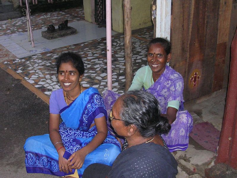 three women in sari sit on the ground and talk to each other