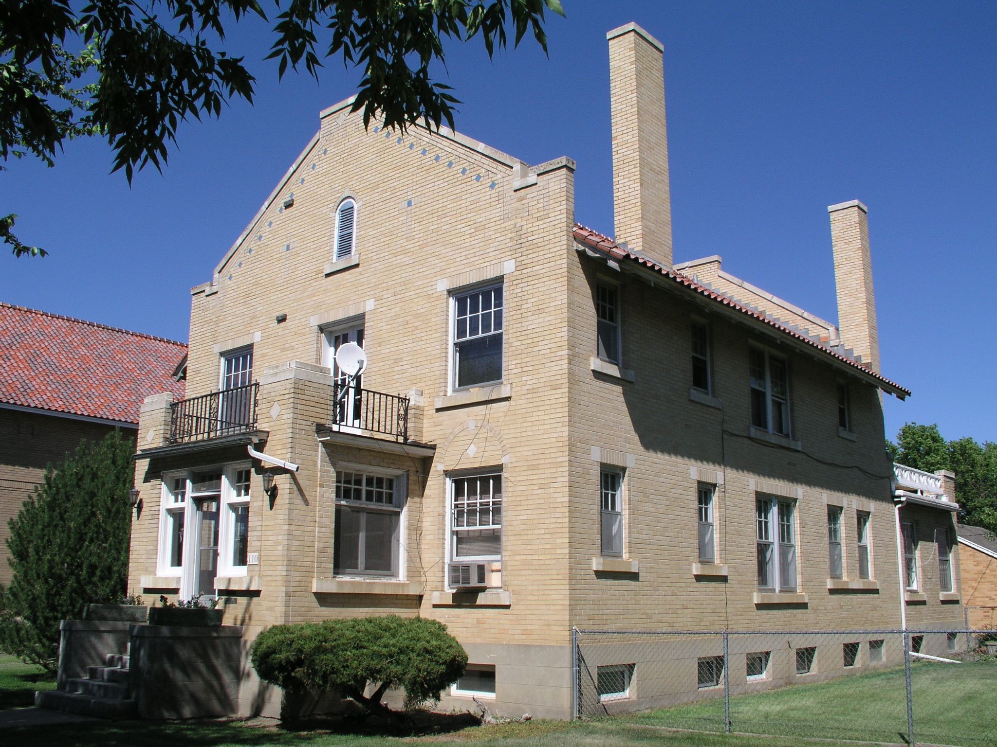 large brick house with three balconies in front of grassy area