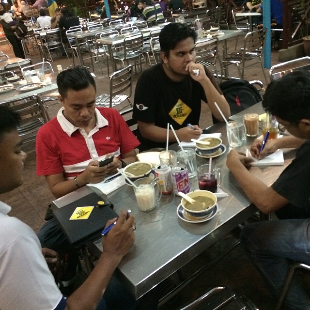 five men sitting at a table eating food and drinking