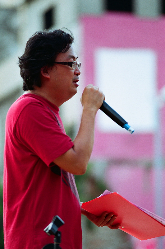 a man holding a microphone stands before a pink building