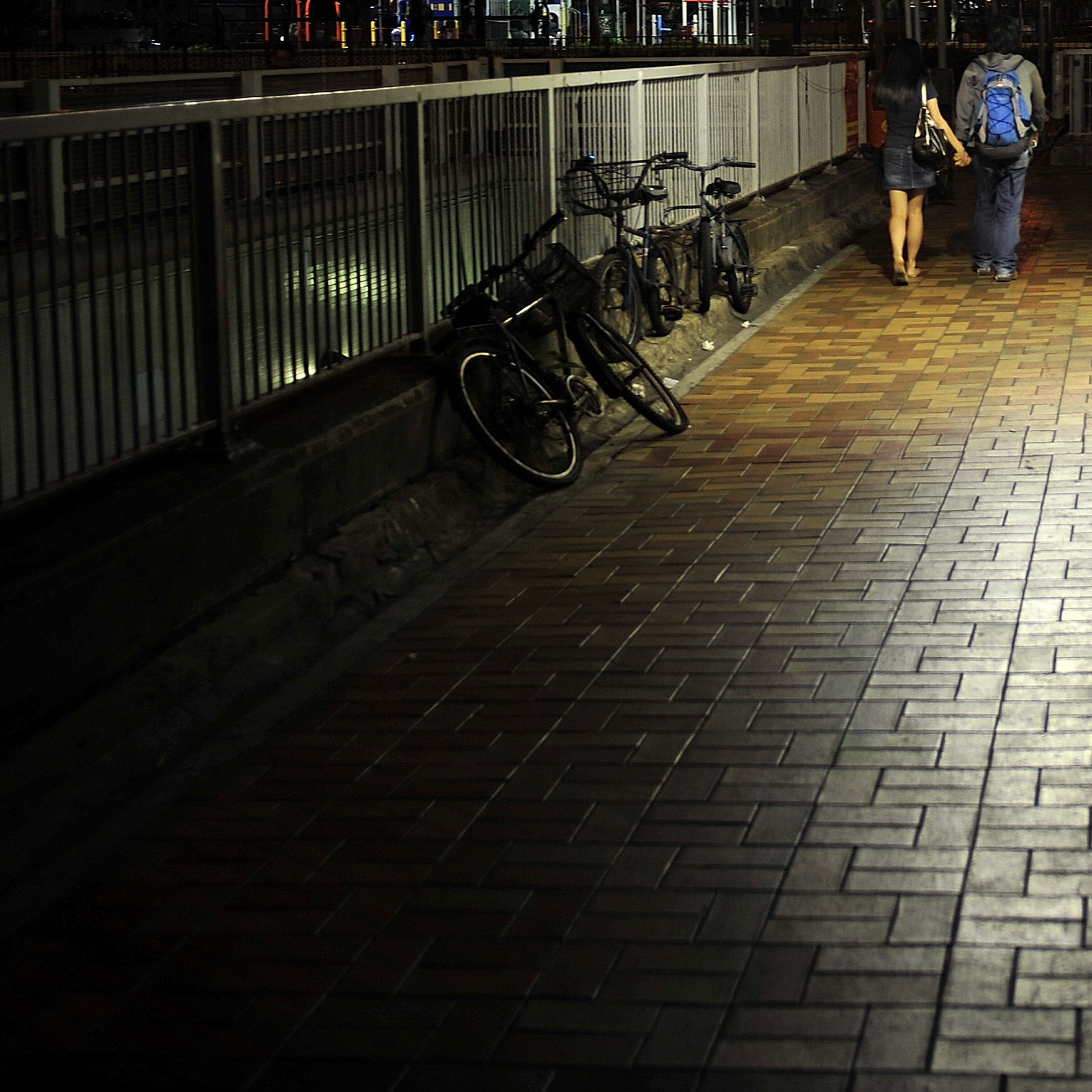 two people walk down the sidewalk with bikes at night