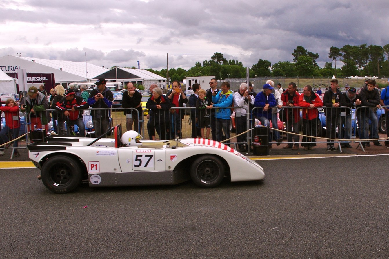 an old race car sits in the middle of a track as many spectators look on