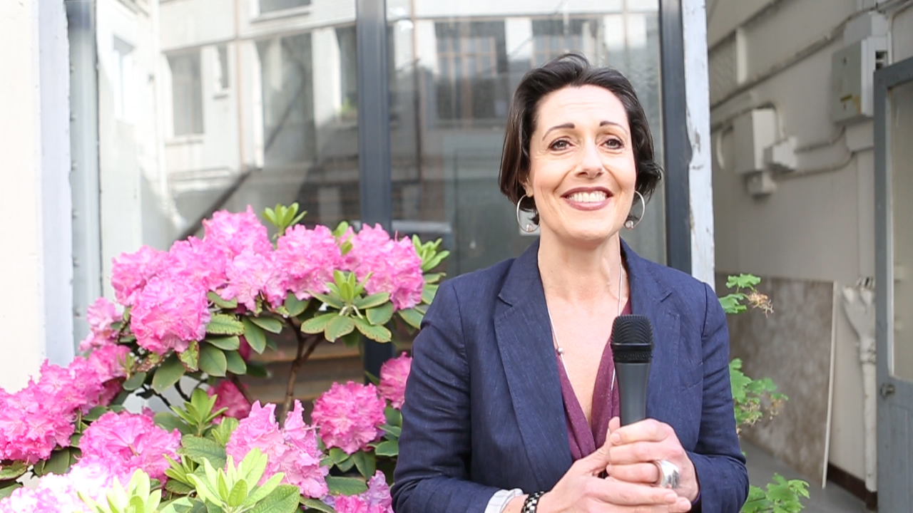 a woman smiling holding a microphone in front of pink flowers