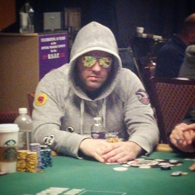 a man in a hoodie playing poker at a green table