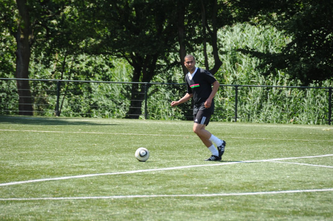 a man in a black shirt kicking a soccer ball on a grass field