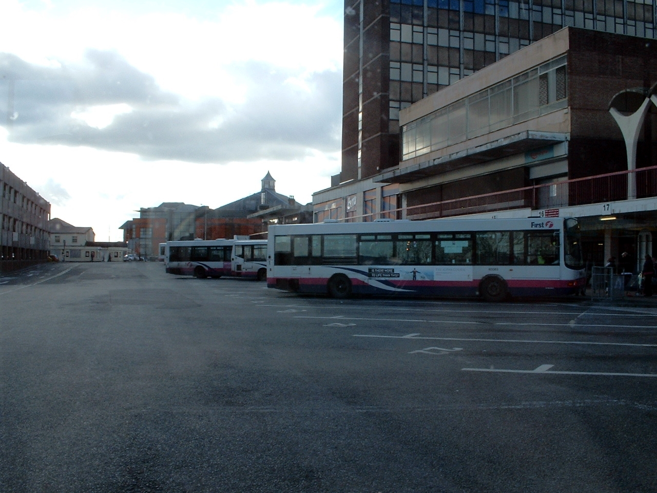 several buses parked at a bus stop and two pedestrians walking away