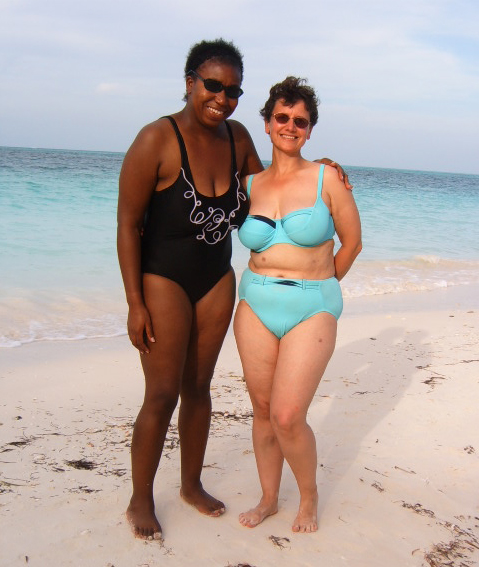 two woman in swimsuits standing on a sandy beach