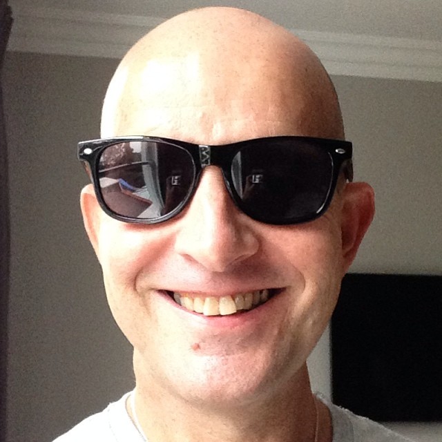 a bald man wearing sunglasses has a white shirt and black tie