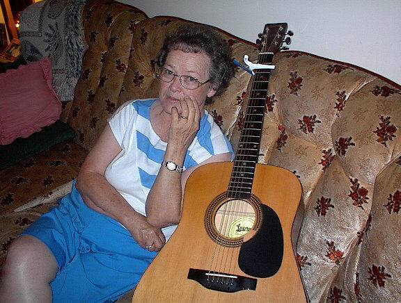 an elderly woman sitting on the couch with a guitar