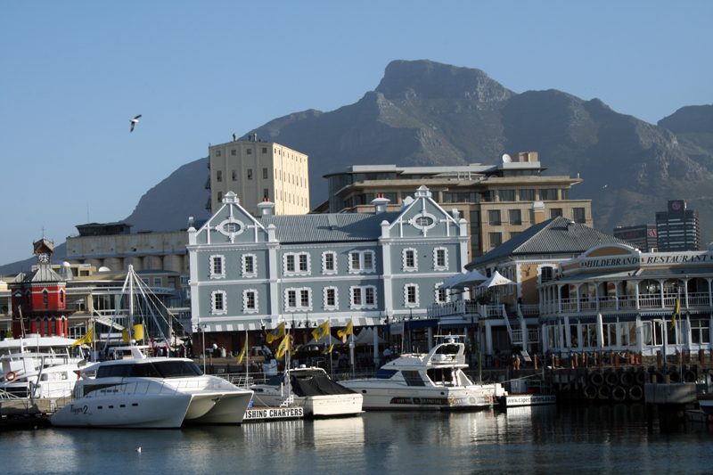 a few buildings near some water with mountains in the background