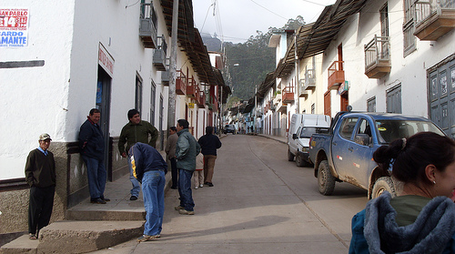 many people are walking down the street by cars