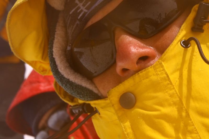 a man standing outdoors wearing a yellow snow suit and goggles