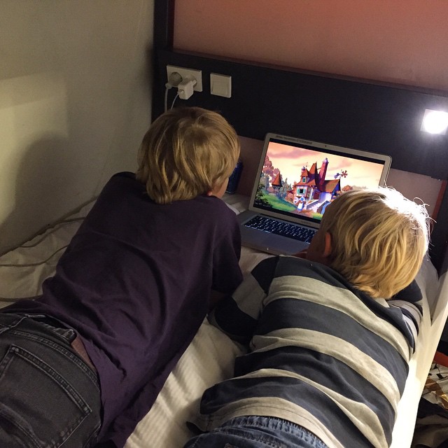 two boys are lying in bed with their laptops