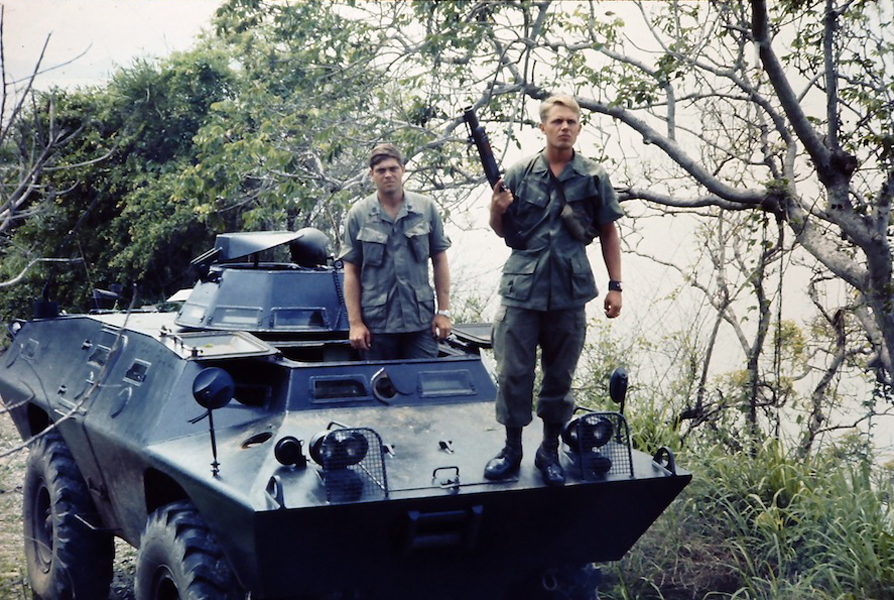 two men are holding guns while standing on an armored vehicle