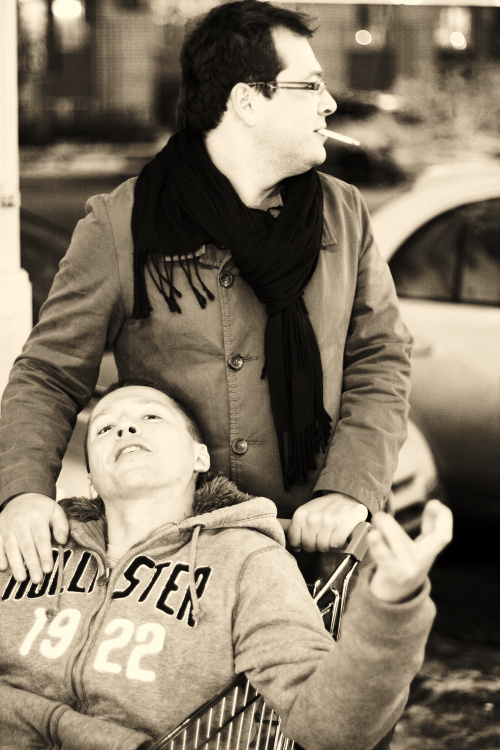 a woman in glasses is hing a shopping cart while a man sits behind her