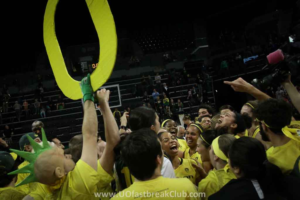 a crowd of people standing on top of a basketball court holding up a yellow ribbon