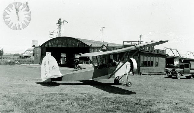 an airplane on a field with buildings in the background