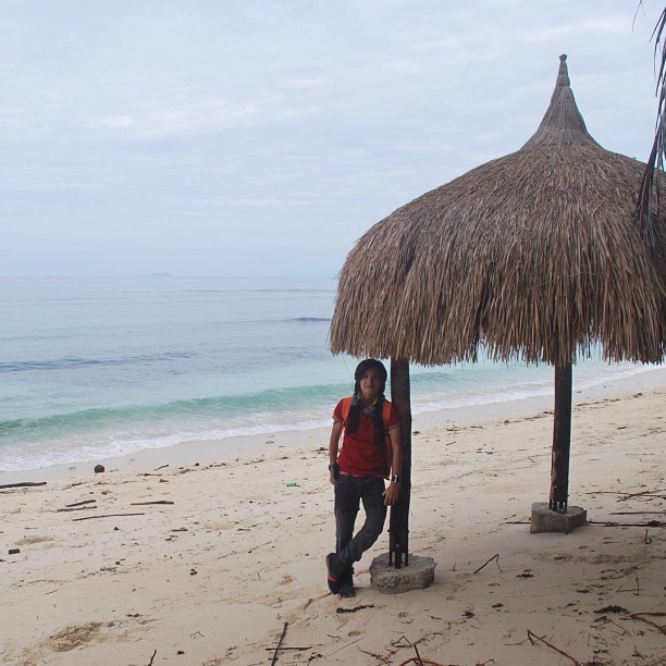 a woman standing on the beach under a thatch roofed hut