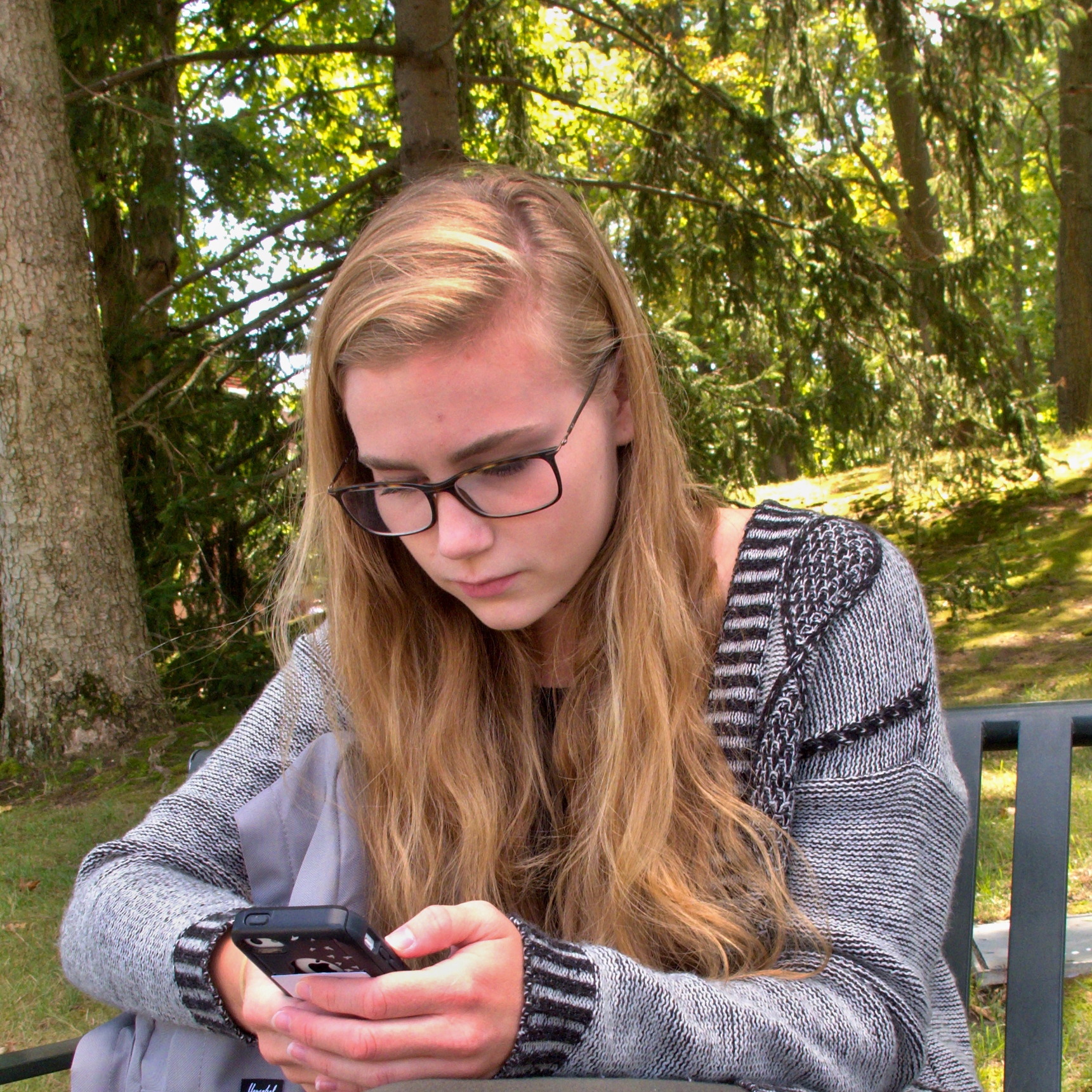 a girl sitting on a park bench looking at her cell phone