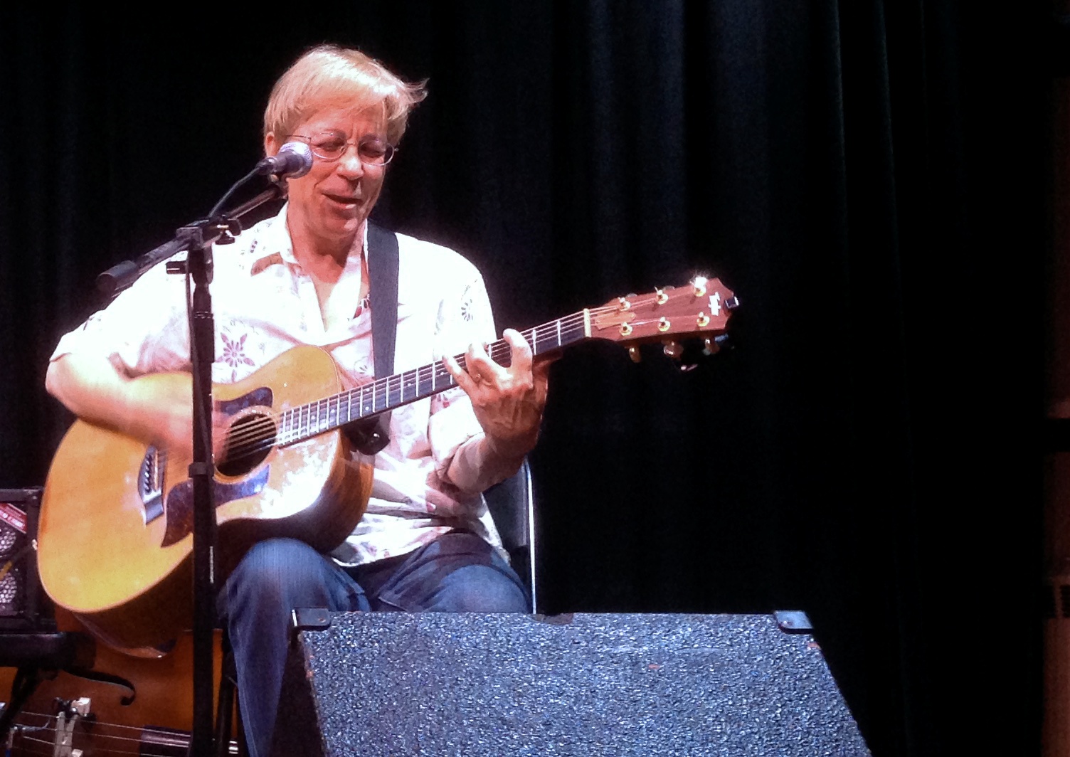 a man with glasses playing the guitar in front of a microphone