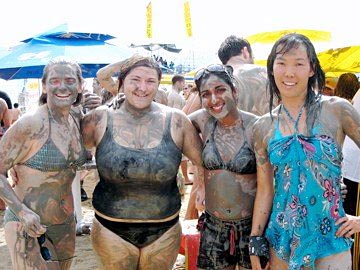 two woman in bathing suits are covered with mud while others are on the other side