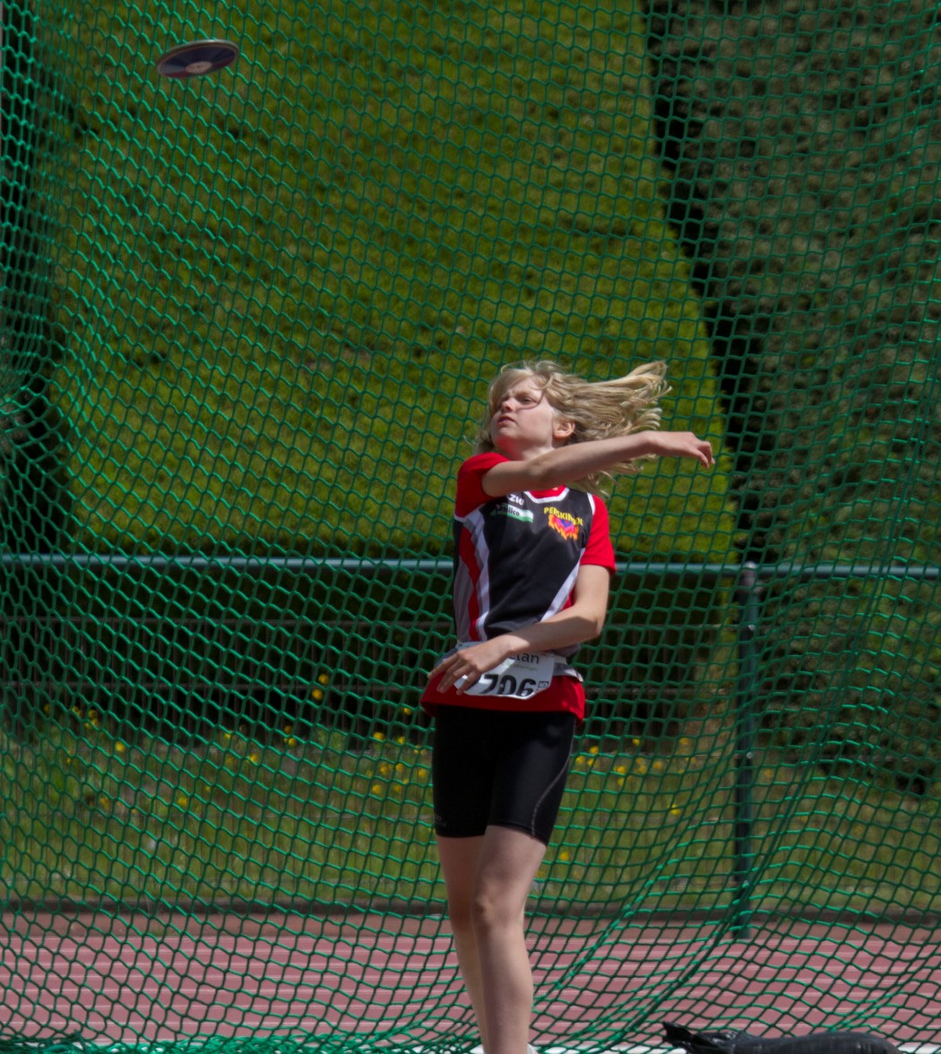 the girl is throwing the frisbee while standing in front of the net