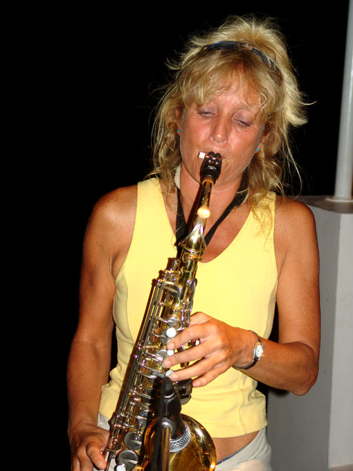 a woman wearing a yellow tank top and playing a saxophone