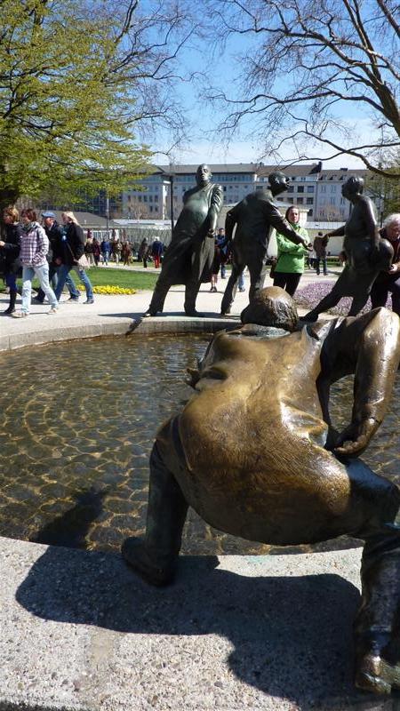 a park with people walking around it and statue in front