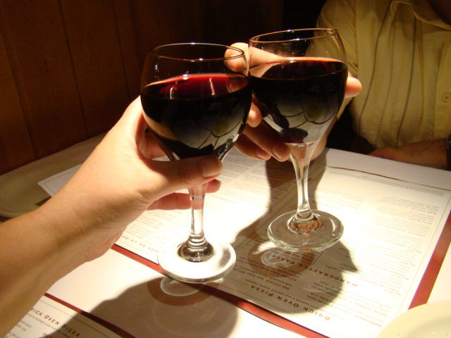 two people holding glasses of red wine in front of a menu