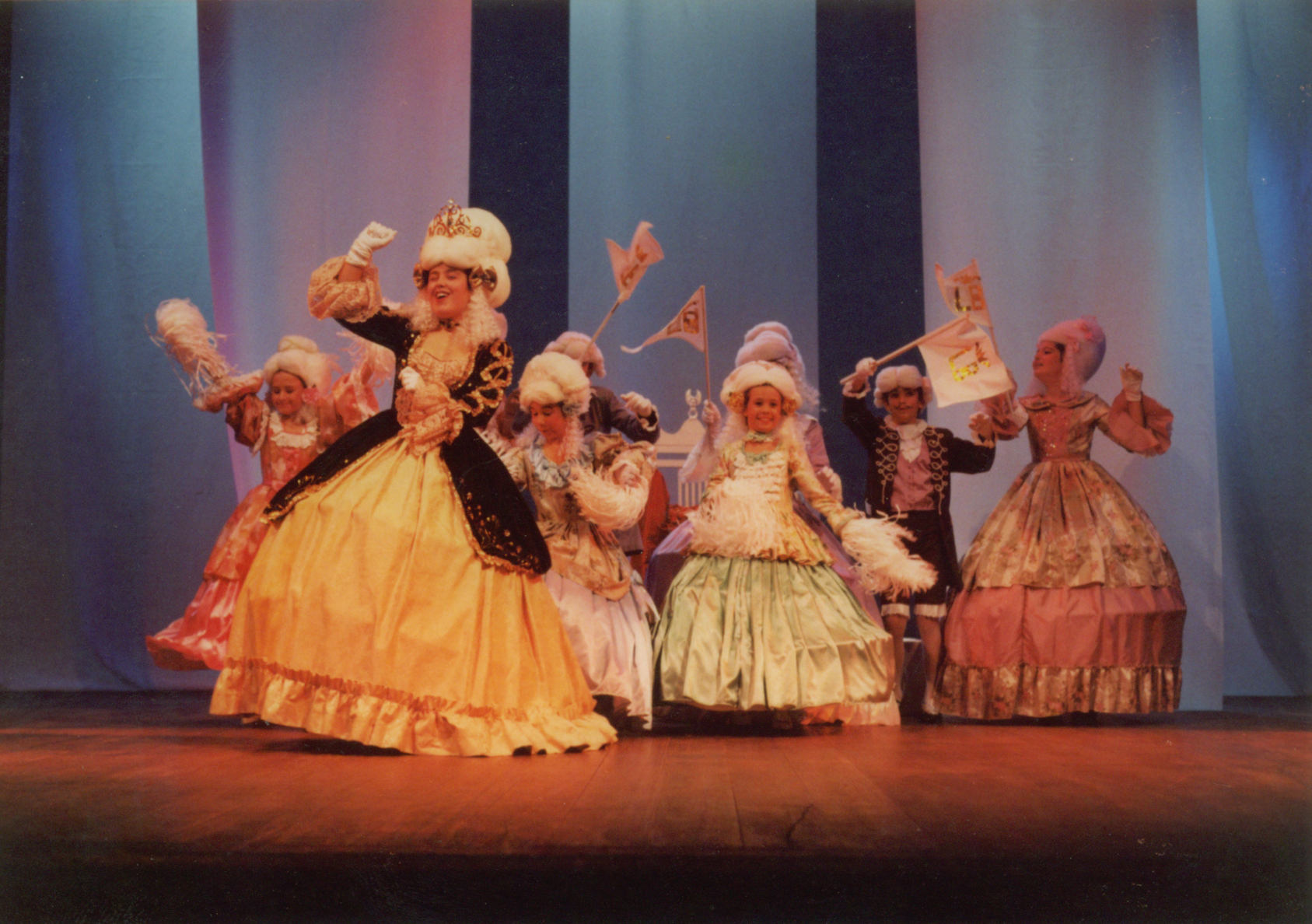 five women in evening dresses stand on a stage