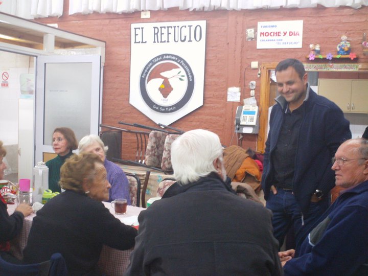 an older man in the background talks to elderly people at a table