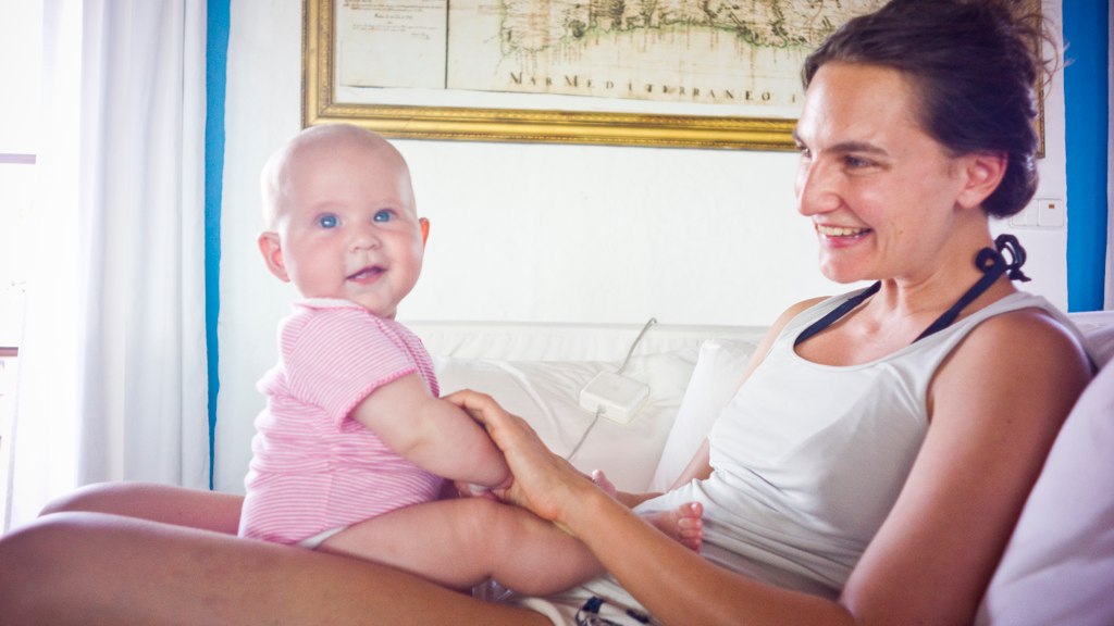 a girl holding a smiling baby while sitting on the bed