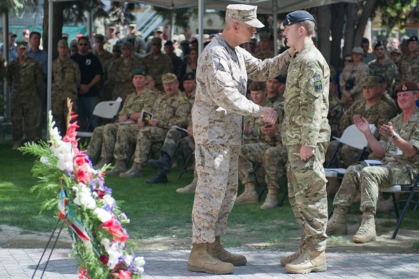 two army men shake hands over a medal