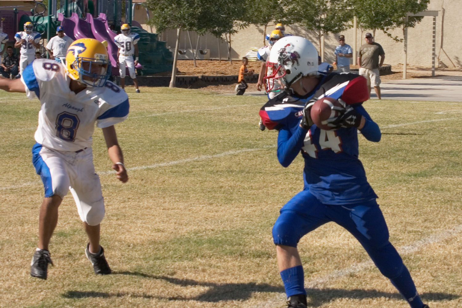 three young people playing football in uniform on a field