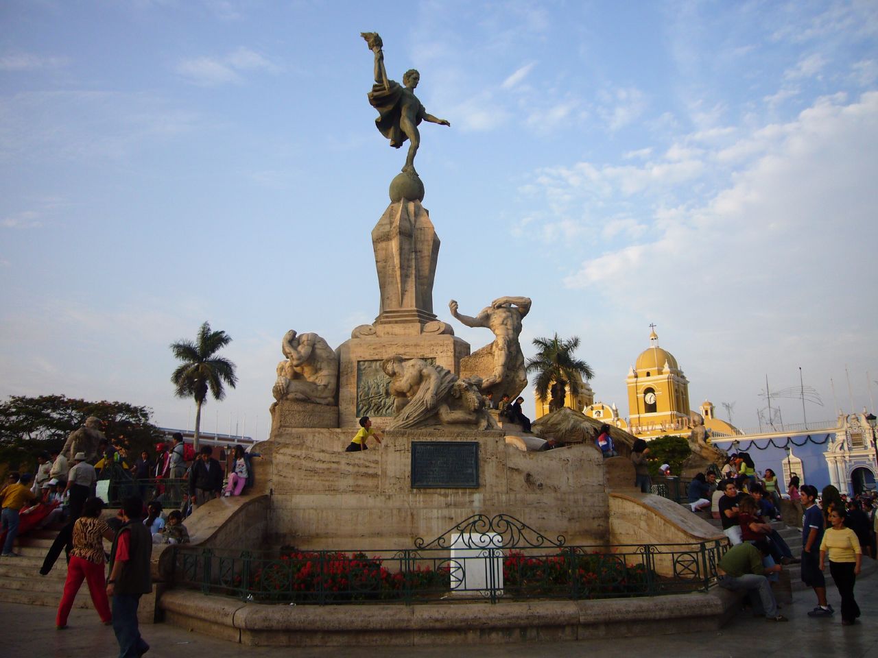 many people are walking around a fountain with a sculpture