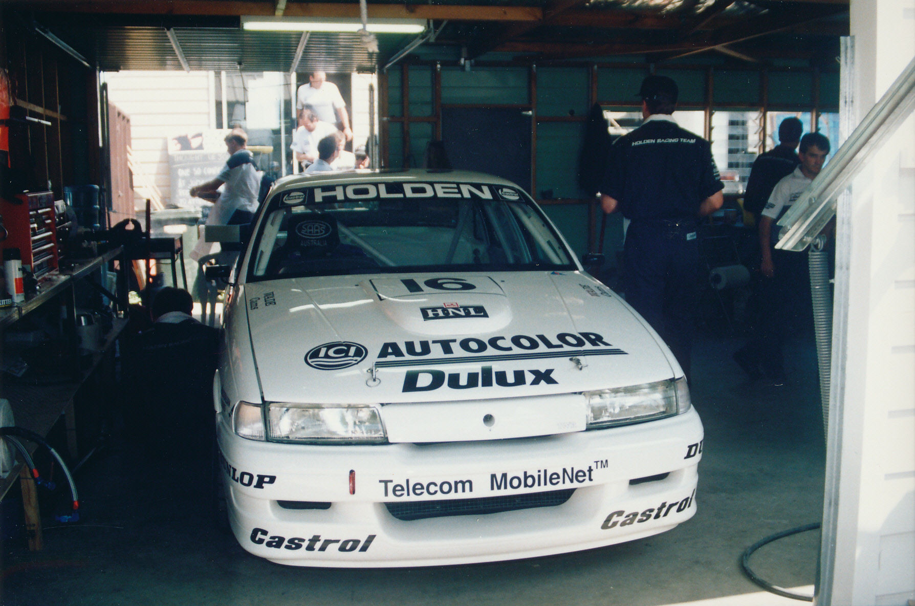 a white car parked inside of a garage with mechanics working on it