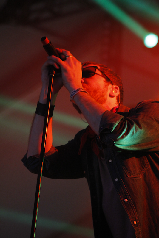 man singing into microphone on stage with green lighting