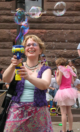 woman with purple and blue dress, holding up a blow - maker