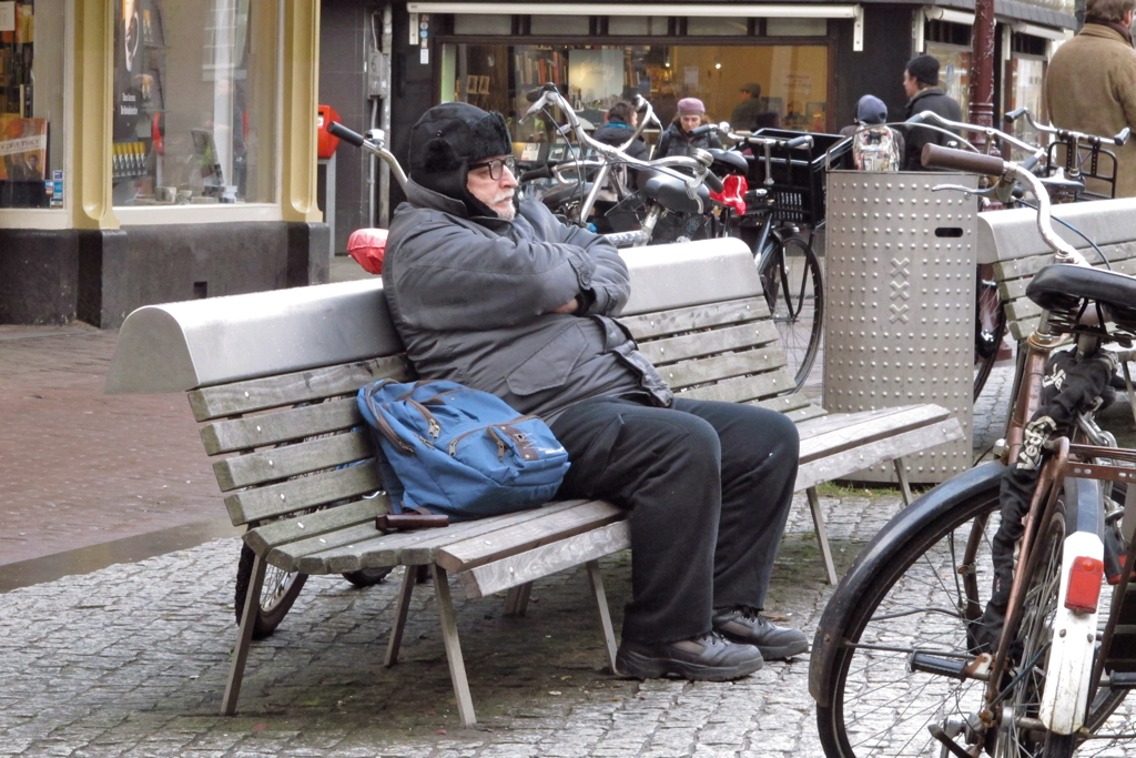 a person with a blue bag on their shoulders sitting on a bench in a busy area