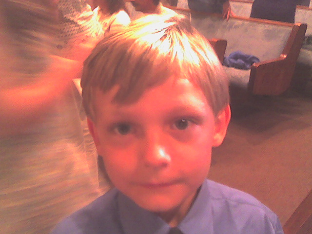 a little boy in a blue dress shirt and tie with his eyes shut