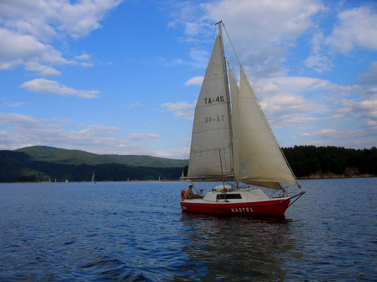 a sailboat floats on the still water with blue sky and clouds