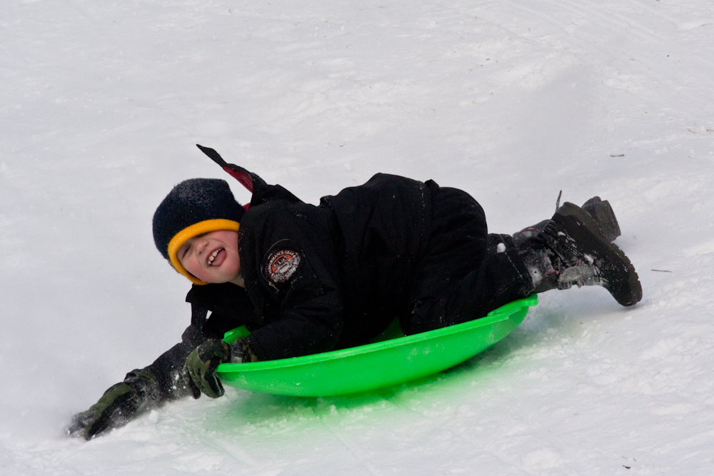 a boy smiles on his back while sledding down a hill